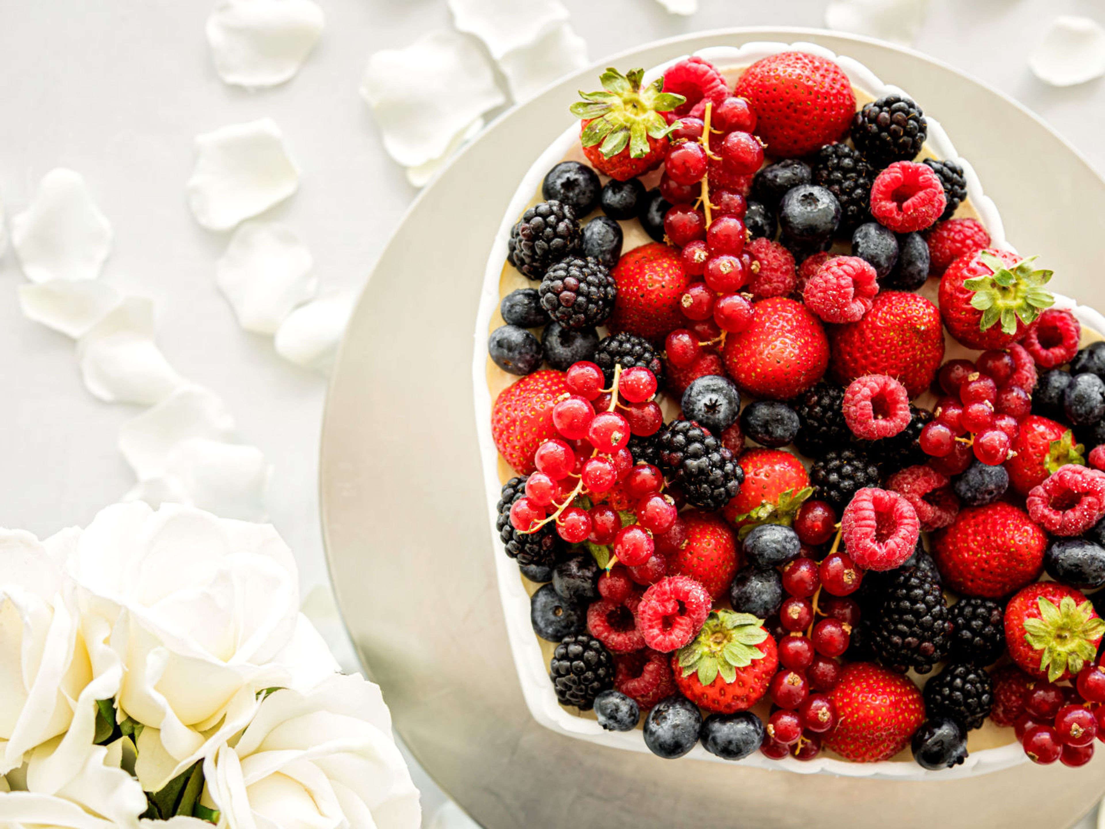 Herzförmige Beeren-Torte mit weißen Rosen und Blütenblättern. Herzförmige Beeren-Torte mit weißen Rosen und Blütenblättern.