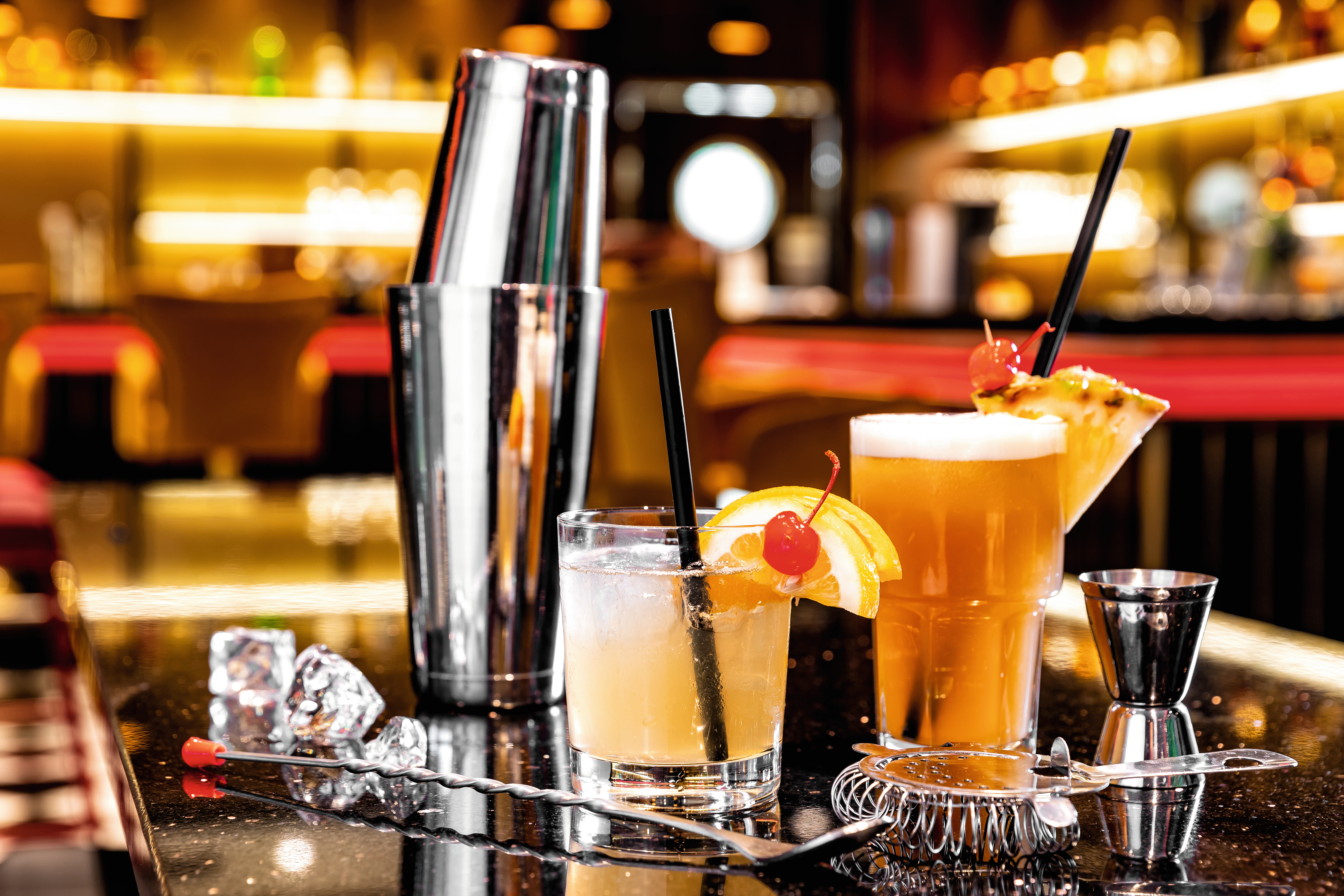 Cocktails mit Früchten und Shaker auf glänzendem Tresen.