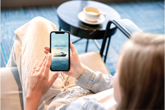 Person entspannt mit Smartphone, Kreuzfahrtschiff der Mein Schiff® Flotte, Kaffeetasse im Hintergrund.