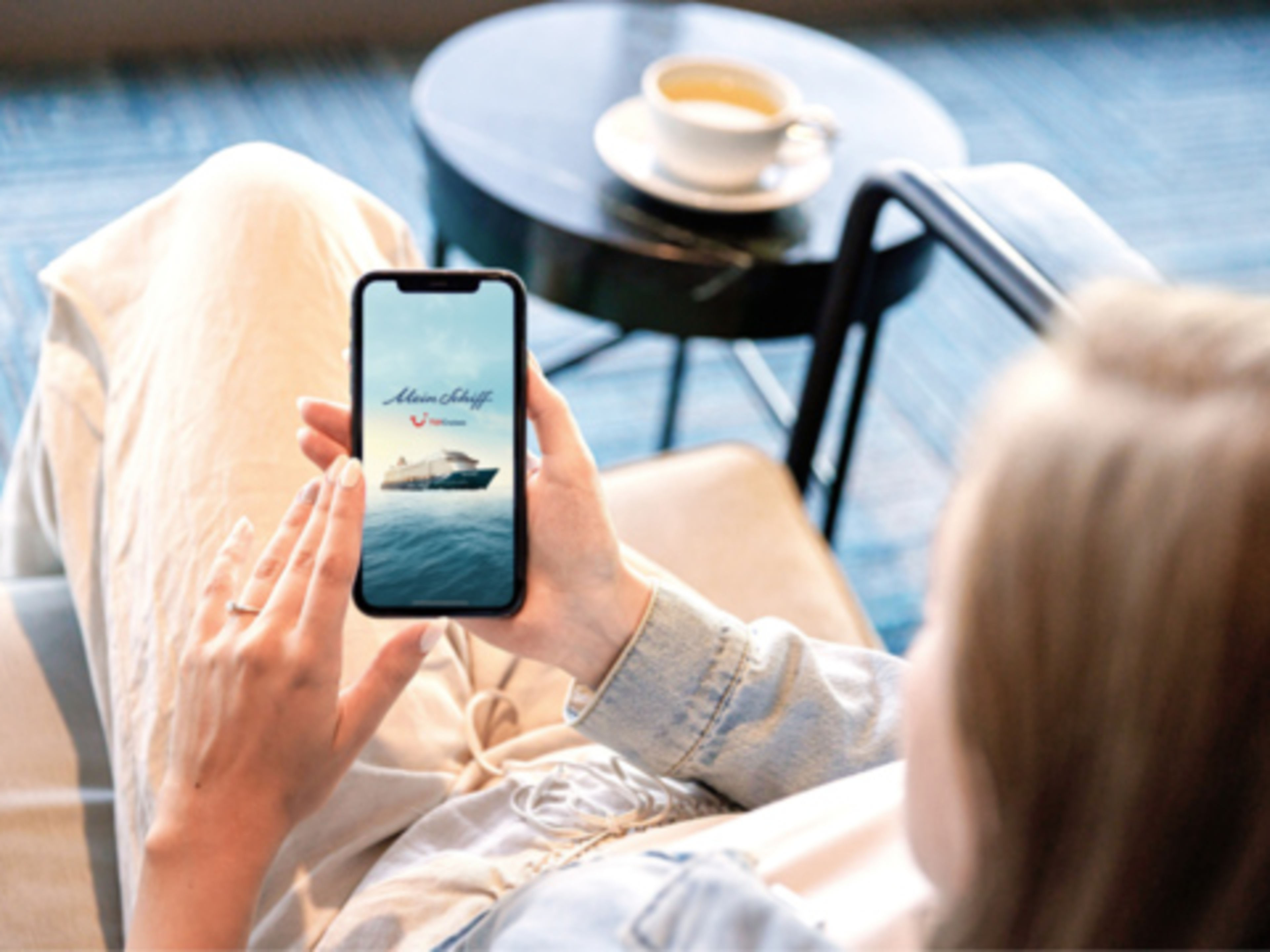 Person entspannt mit Smartphone, Kreuzfahrtschiff der Mein Schiff® Flotte, Kaffeetasse im Hintergrund. Person entspannt mit Smartphone, Kreuzfahrtschiff der Mein Schiff® Flotte, Kaffeetasse im Hintergrund.