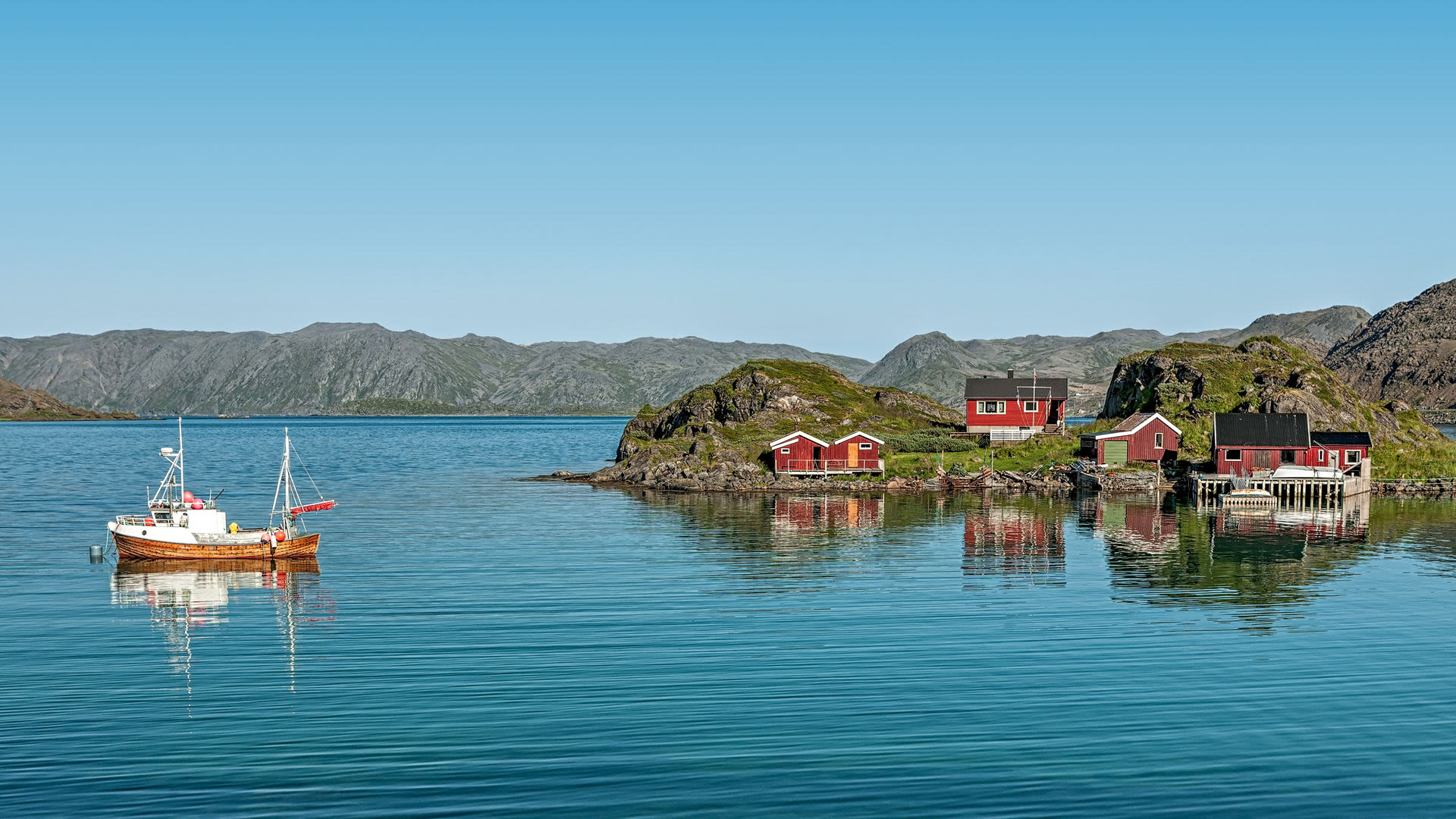 Fischerboot und rote Hütten am Fjord in Norwegen.