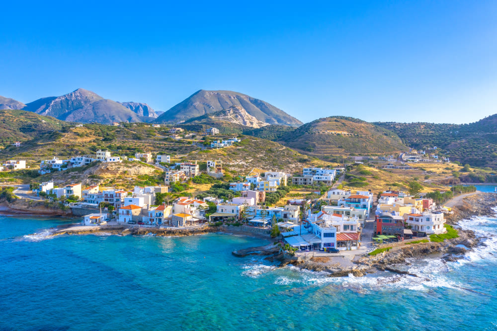 Küstenstadt auf Kreta mit bunten Häusern und Bergen im Hintergrund.
