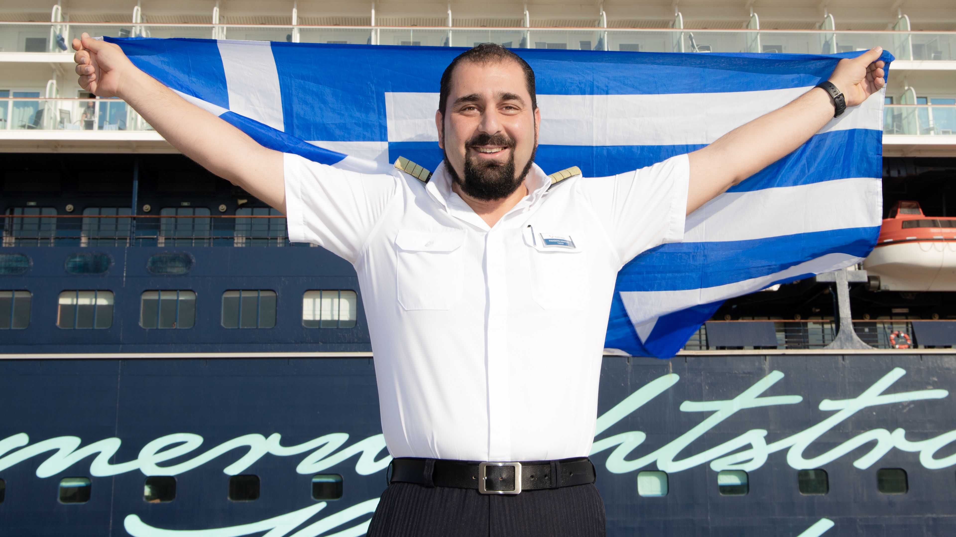 Mann in Uniform hält griechische Flagge vor Kreuzfahrtschiff der Mein Schiff® Flotte. Mann in Uniform hält griechische Flagge vor Kreuzfahrtschiff der Mein Schiff® Flotte.