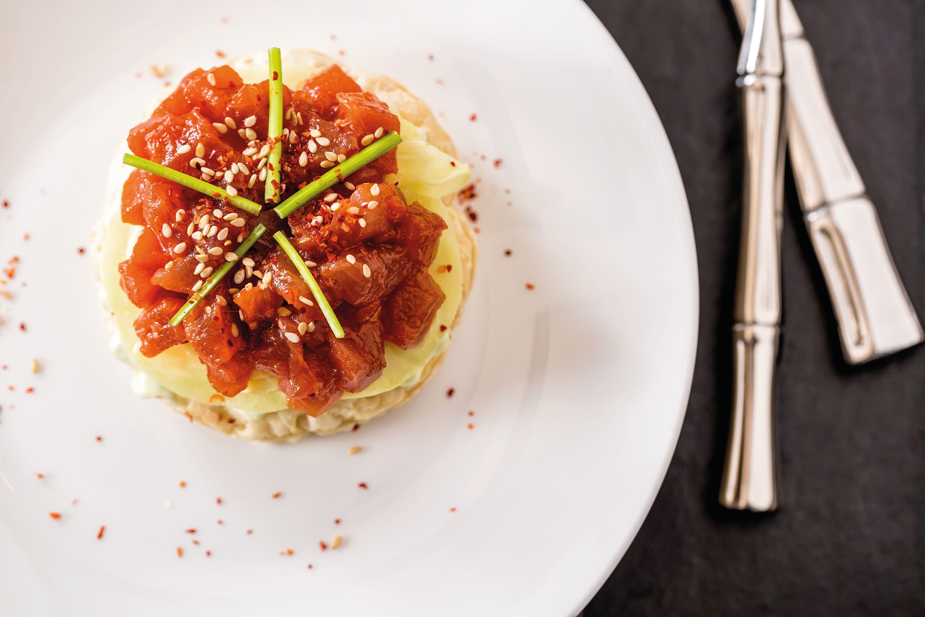 Gourmet starter: Japanese pizza with salmon, sesame seeds and chives, served on a white plate.