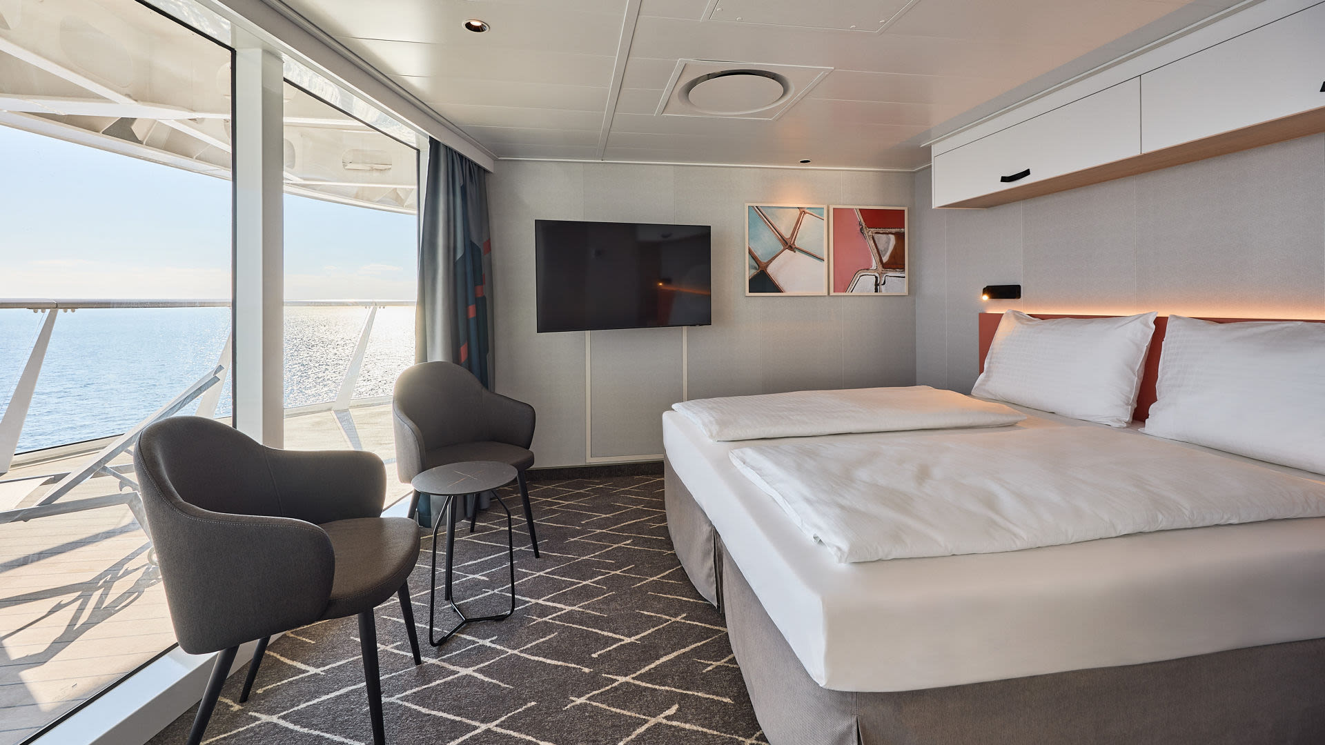 Kreuzfahrtschiff-Kabine mit Doppelbett, Meerblick, grauen Sesseln und moderner Dekoration.