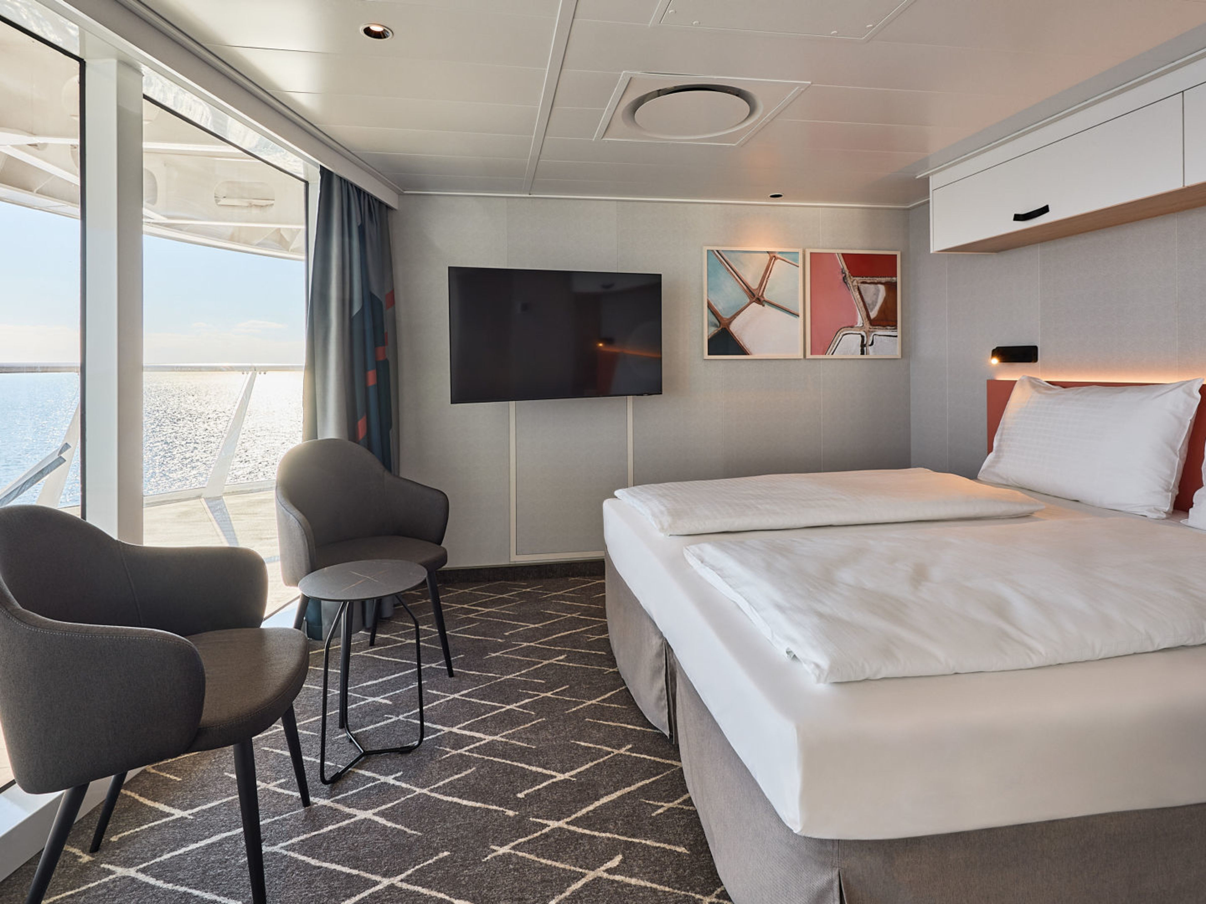 Kreuzfahrtschiff-Kabine mit Doppelbett, Meerblick, grauen Sesseln und moderner Dekoration. Kreuzfahrtschiff-Kabine mit Doppelbett, Meerblick, grauen Sesseln und moderner Dekoration.