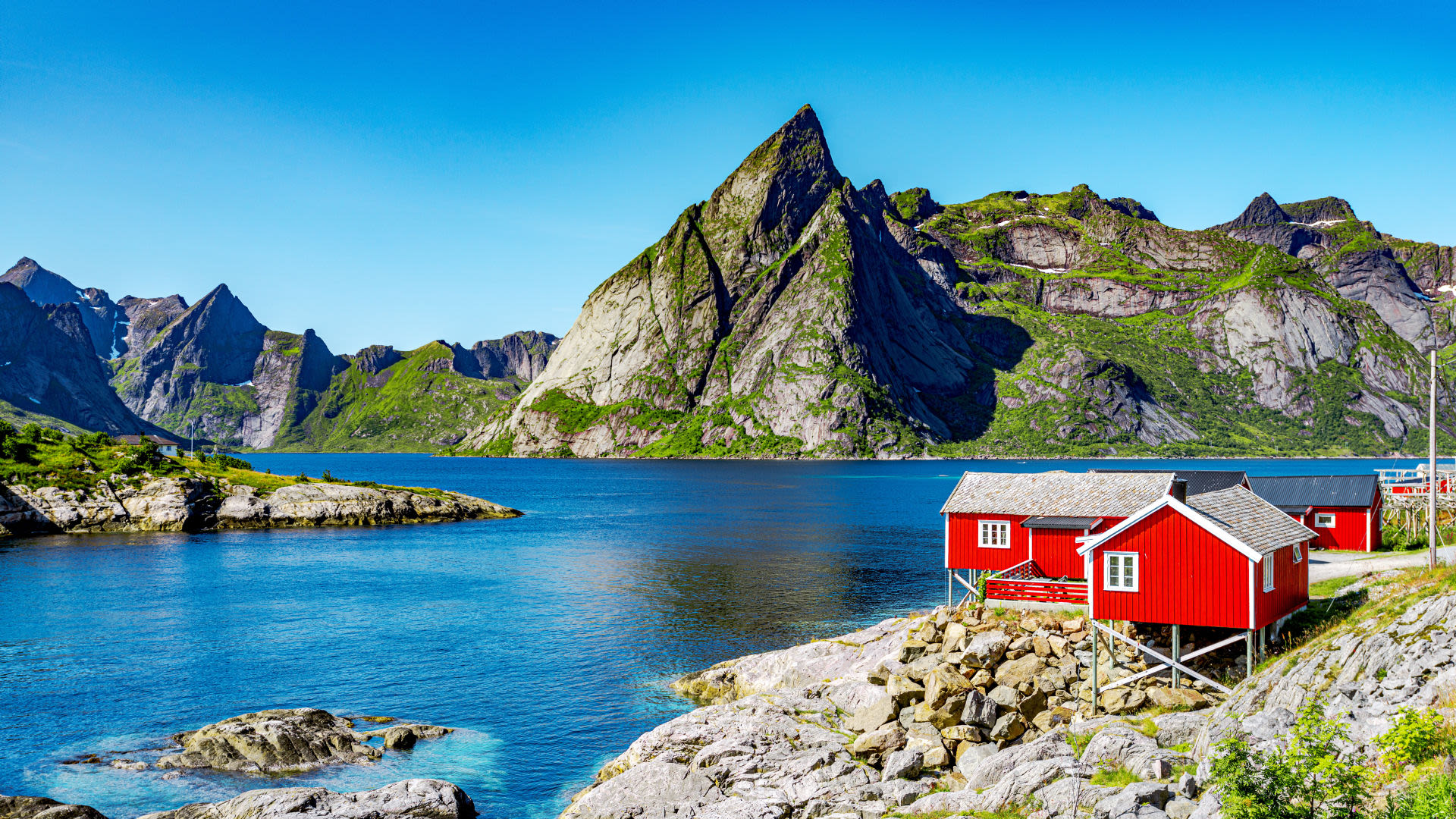 Rote Häuser am Fjord vor steilen Bergen, Lofoten.