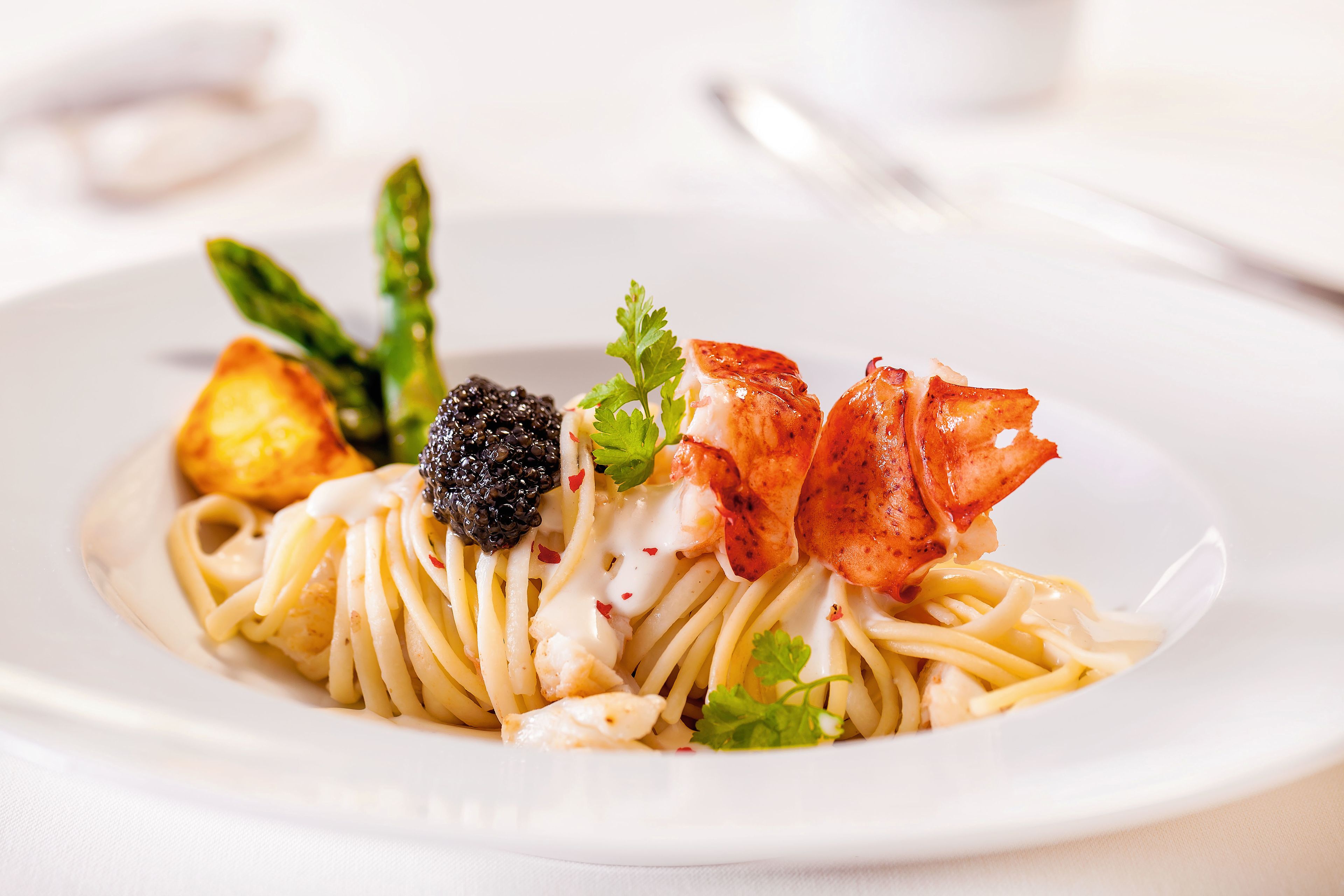 Spaghetti mit Hummer, Kaviar, Spargel und Kartoffel auf weißem Teller.