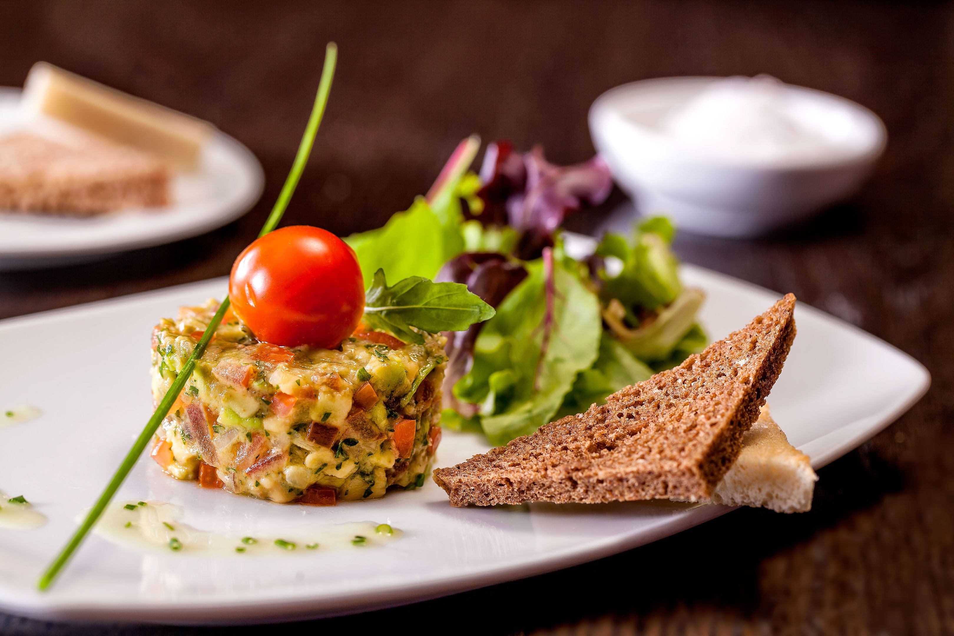 Gourmet-Vorspeise mit Tomate, Salat und Brot auf weißem Teller.