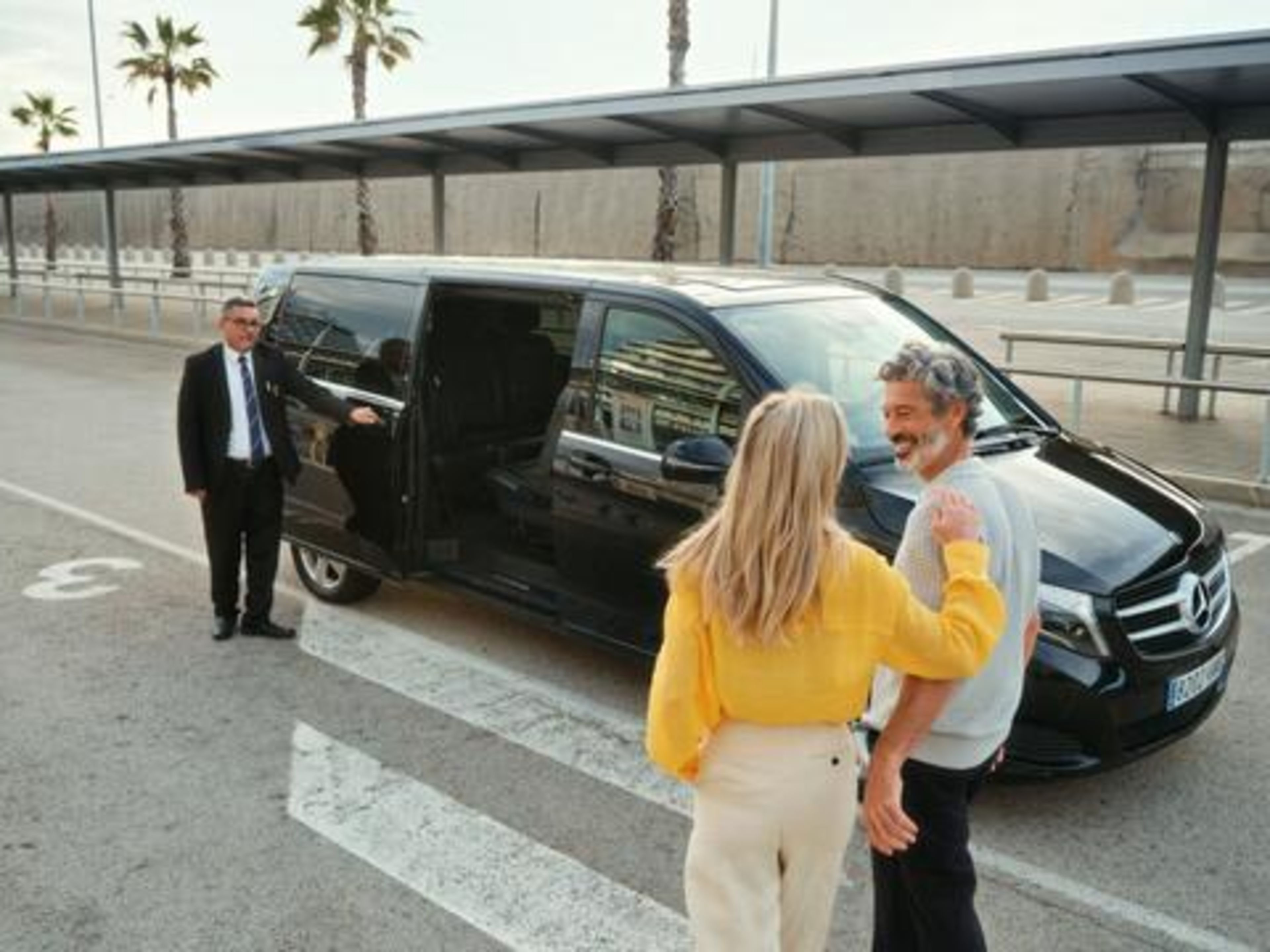 Paar begrüßt Fahrer vor schwarzem Mercedes-Van an sonnigem Flughafen. Paar begrüßt Fahrer vor schwarzem Mercedes-Van an sonnigem Flughafen.