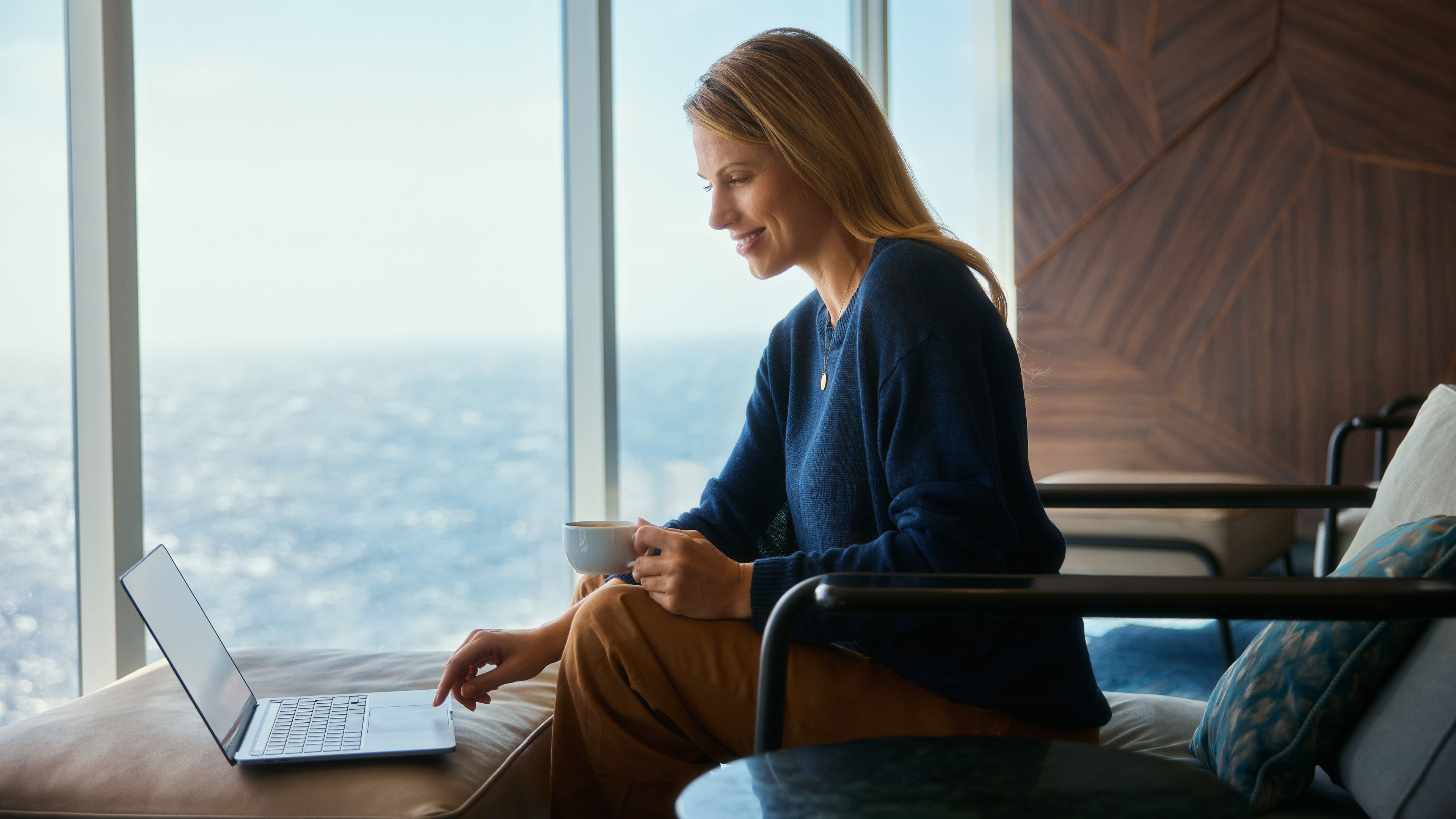Frau am Laptop mit Kaffeetasse, Meerblick im Hintergrund. Frau am Laptop mit Kaffeetasse, Meerblick im Hintergrund.