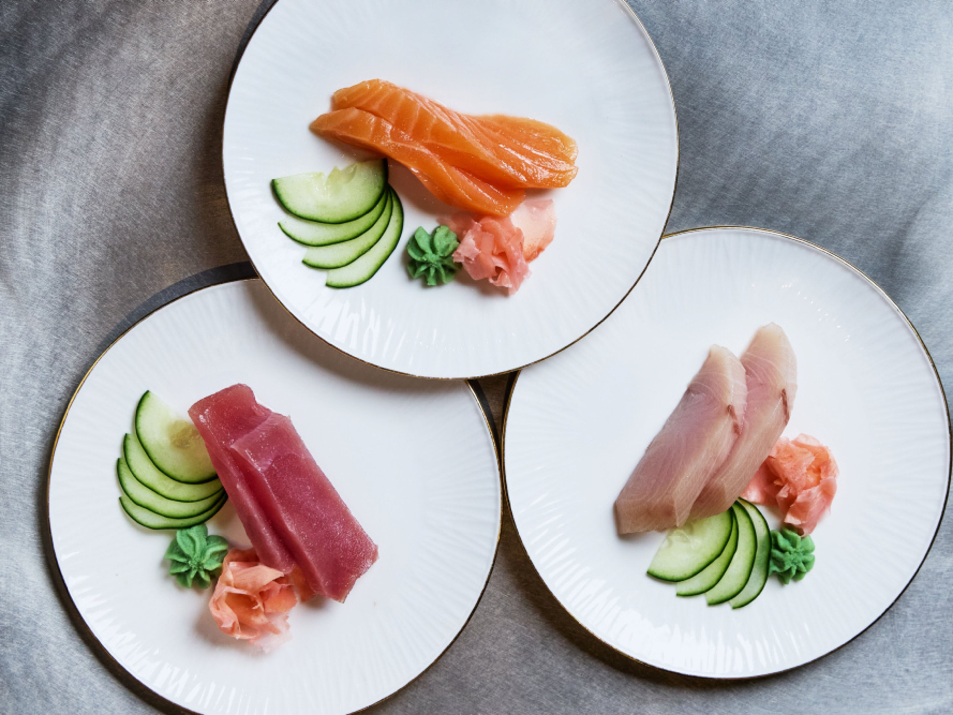 Drei Teller mit Sashimi, Gurken, Wasabi und Ingwer auf grauem Hintergrund. Drei Teller mit Sashimi, Gurken, Wasabi und Ingwer auf grauem Hintergrund.